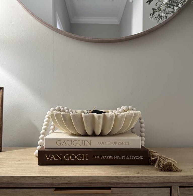 Scalloped decorative bowl on stacked art books with wood beads on a console table.