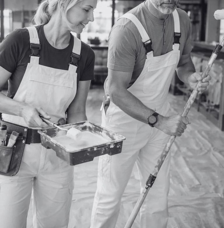 a man and woman in white overalls holding a paintbrush and paint roller