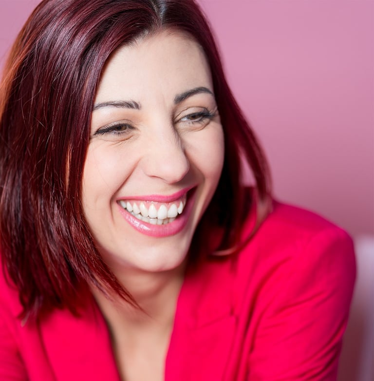 Portrait d’une comédienne qui rit, en veste rose sur fond rose, sourire naturel et expressif.