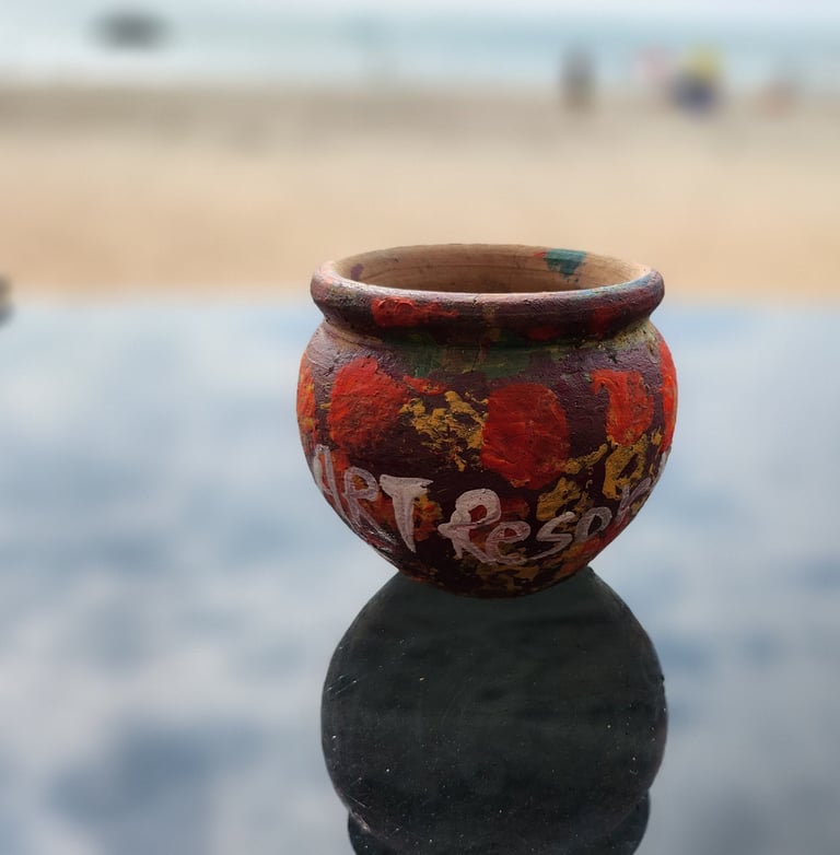 Hand-painted clay pot with colorful patterns reflecting on a glass table at a beach resort.