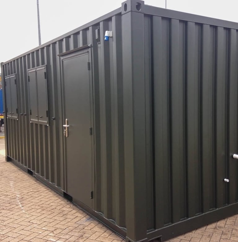 Dark green modified shipping container office with a steel door and side windows on a paved area.