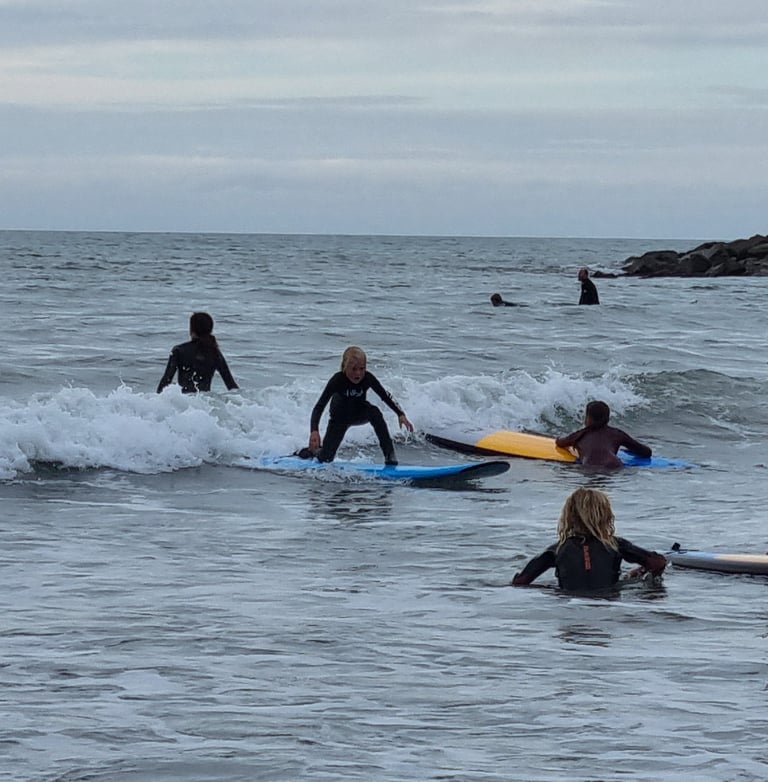 A busy after school surf club lesson with a young male surfer an a wave other children watching