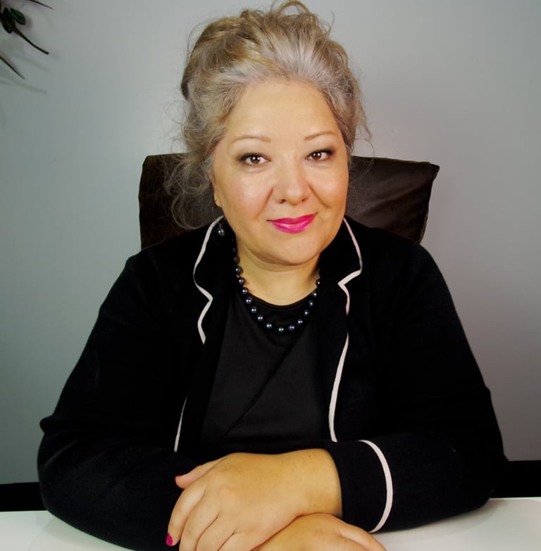 Professional businesswoman with grey hair and pink lipstick wearing a black blazer in an office setting.
