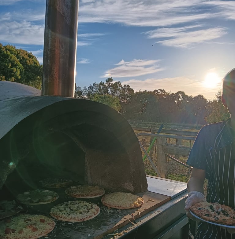 Our waiter next to a pizza oven, at a party with a sunset in the background