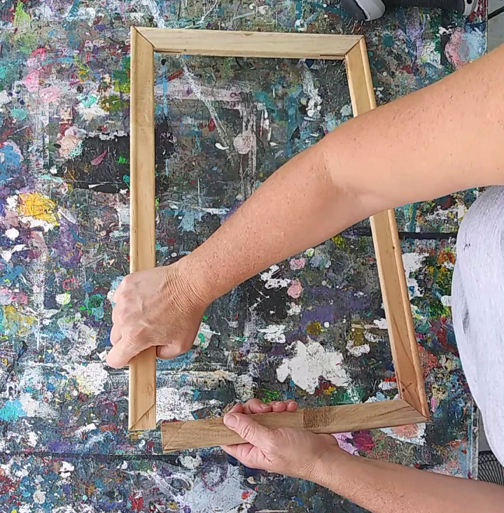 a person holding a wooden frame with a painting on it
