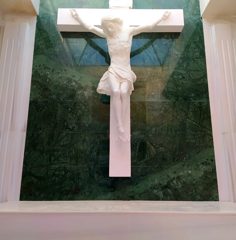 White marble sculpture of Jesus on a crucifix mounted on a green stone wall inside a church.