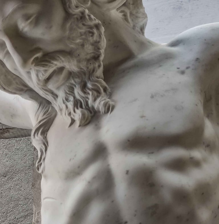 A close-up of a white marble religious sculpture showing the bearded face and torso of Jesus on the cross.