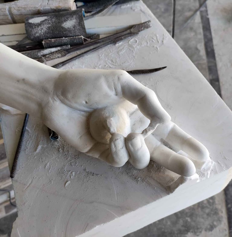 Detailed marble sculpture of a hand holding a small sphere on a stone workbench with carving tools.