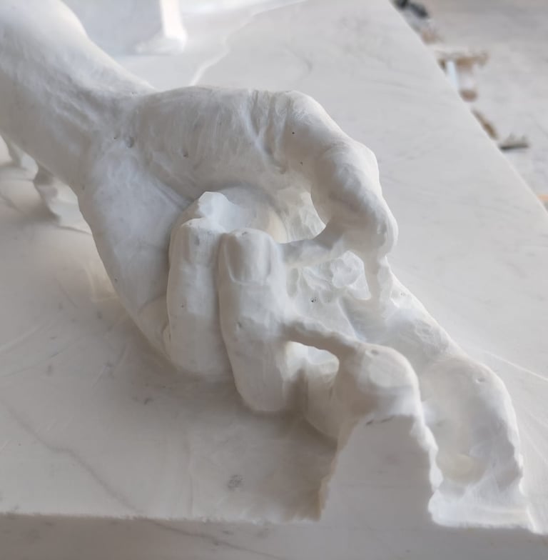 Close-up of a hand being carved from a white marble block in a sculptor's workshop.