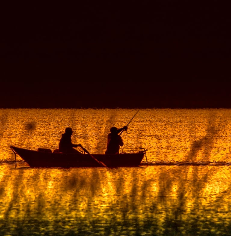 two people fishing in a lake at sunset
