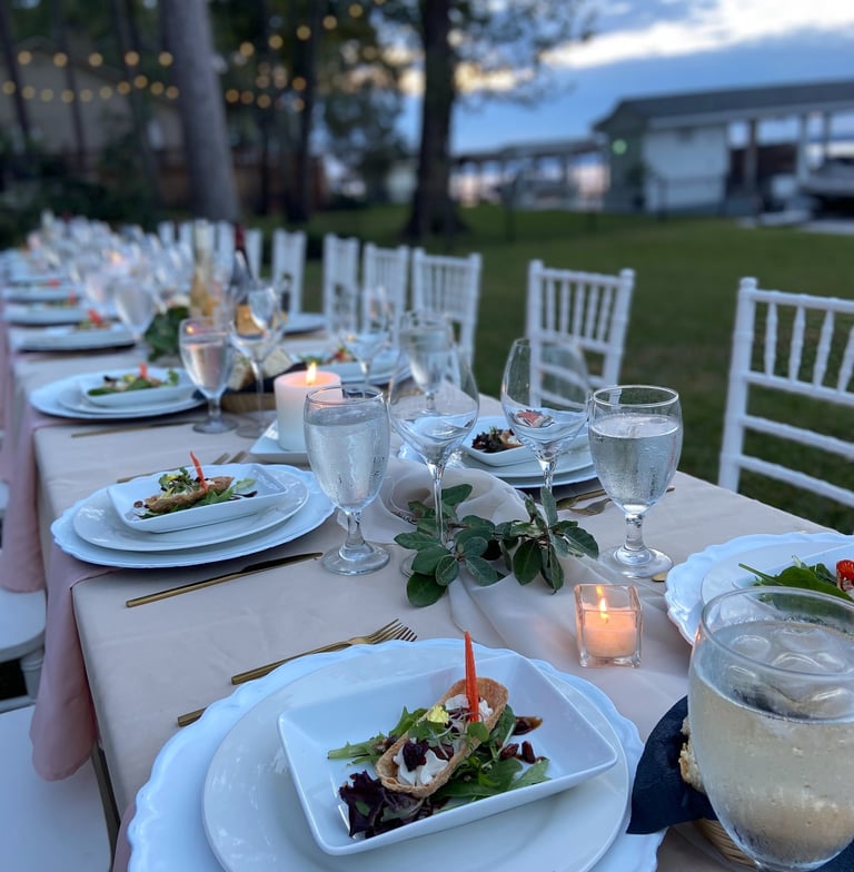 Outdoor al fresco dining table with plates, napkins and cutlery neatly arranged. Candles and flowers