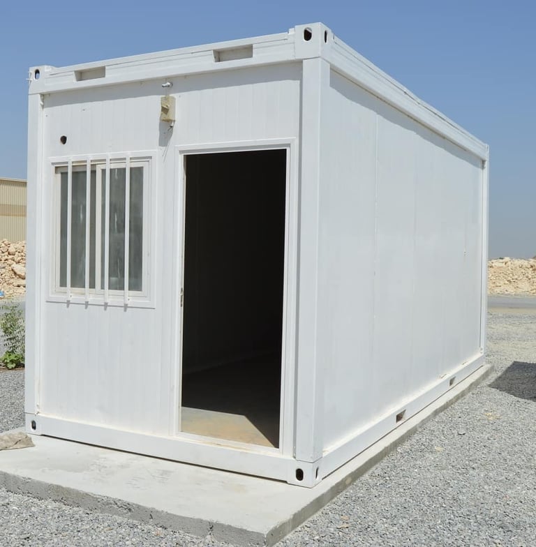 A white portable modular container office with a window and open door on a construction site.