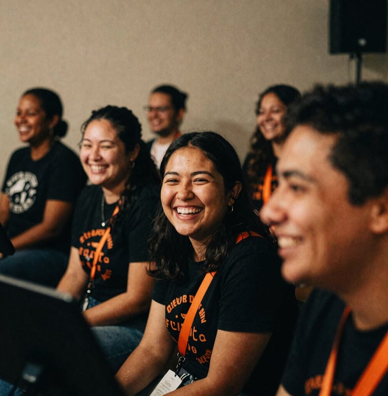 Close-up, slightly off-kilter, gritty film photography of diverse, smiling volunteers sharing a laugh while setting up for a concert in a dimly lit community space, warm beige and deep black tones, vibrant orange accents, 35mm grain.
