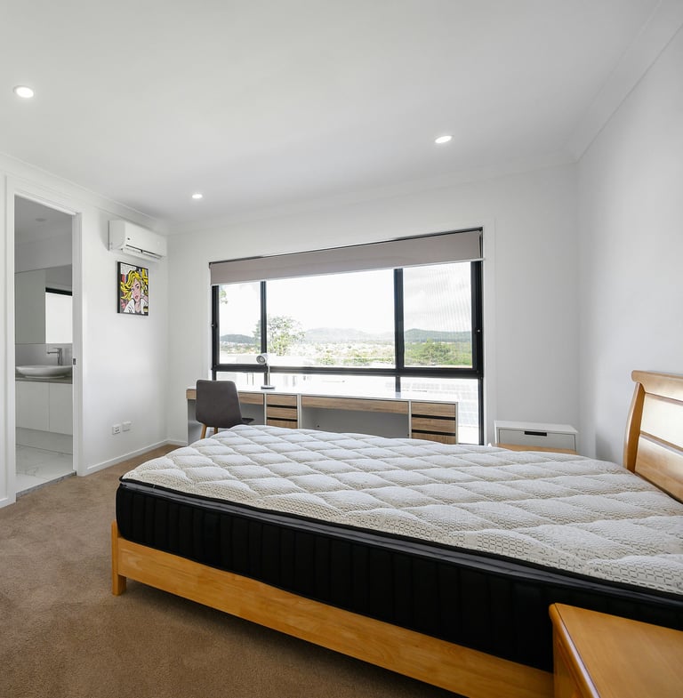 Bright bedroom with a mattress on a wooden frame and large window.