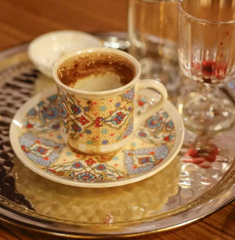 a cup of coffee on a tray with a spoon and a glass of wine