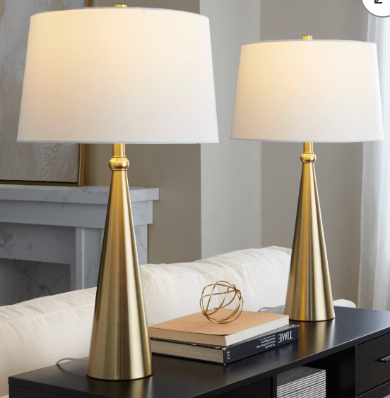 Pair of modern brass table lamps with white drum shades on a black console table in a living room.