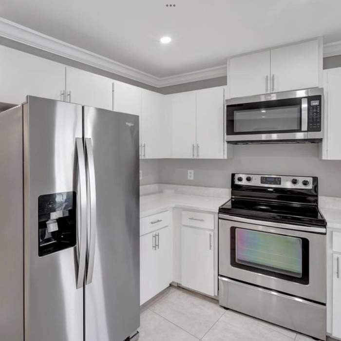 Kitchen remodel with white cabinets and stainless steel refrigerator, microwave, and oven.