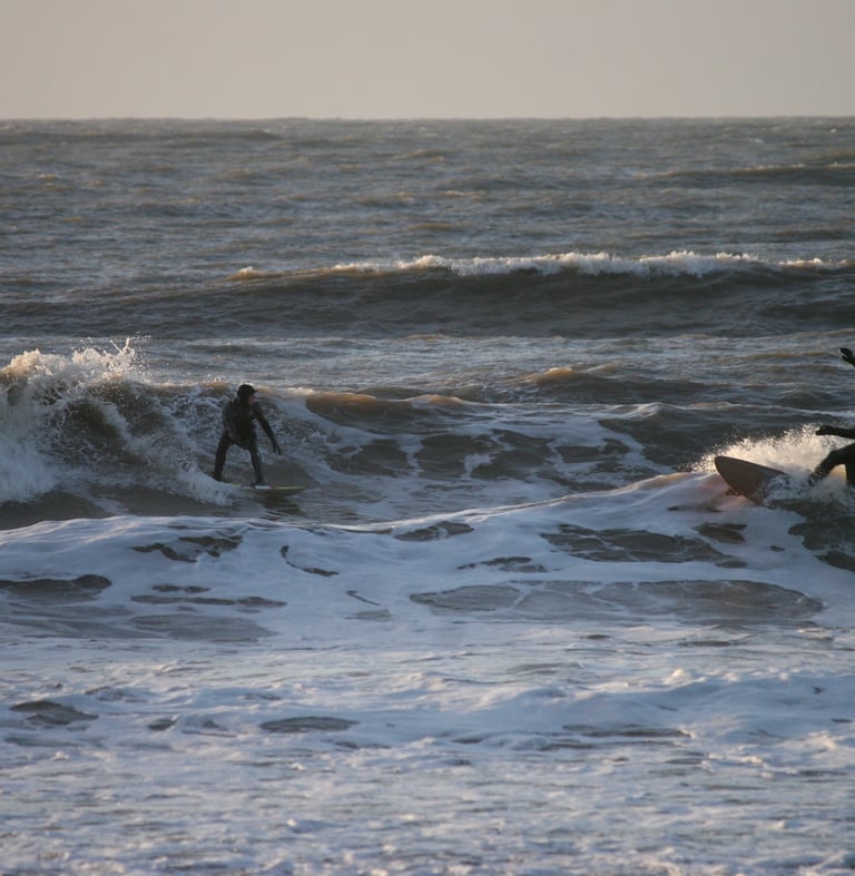 Two surfers riding towards each other in wintery sunshine