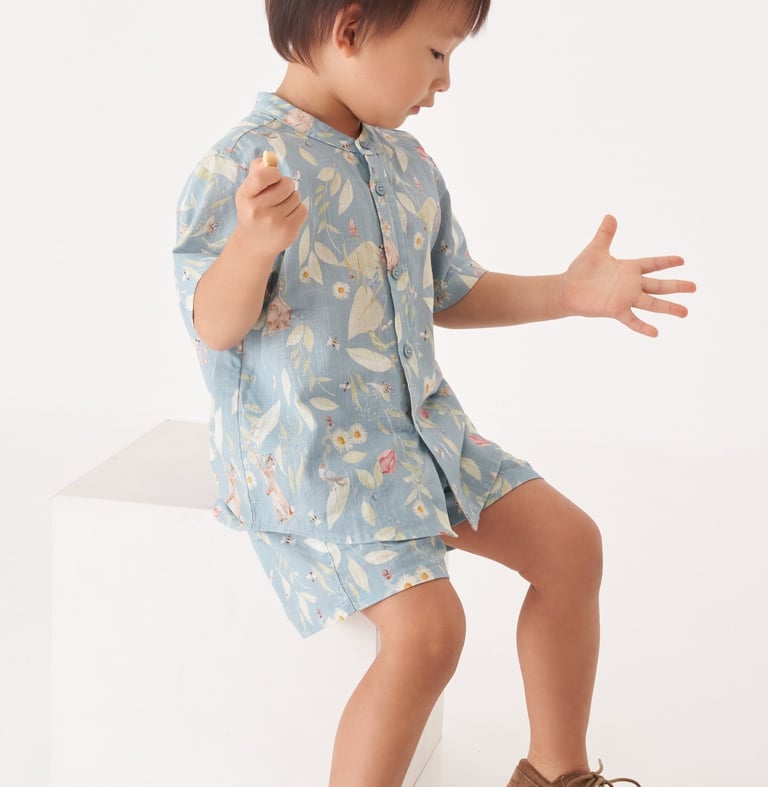 Menino asiático veste roupa com estampa de paisagem natural com animais e plantas