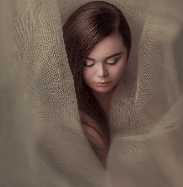 Creative portrait of a young woman wrapped in sheer tulle, creating an ethereal, dreamy effect.