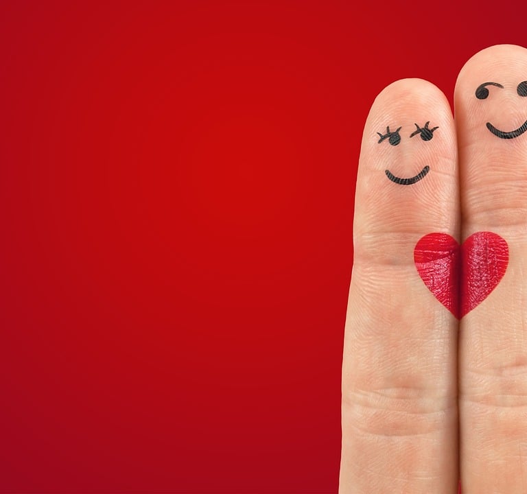 Two fingers with drawn smiley faces and a red heart represent a happy couple on a red background.