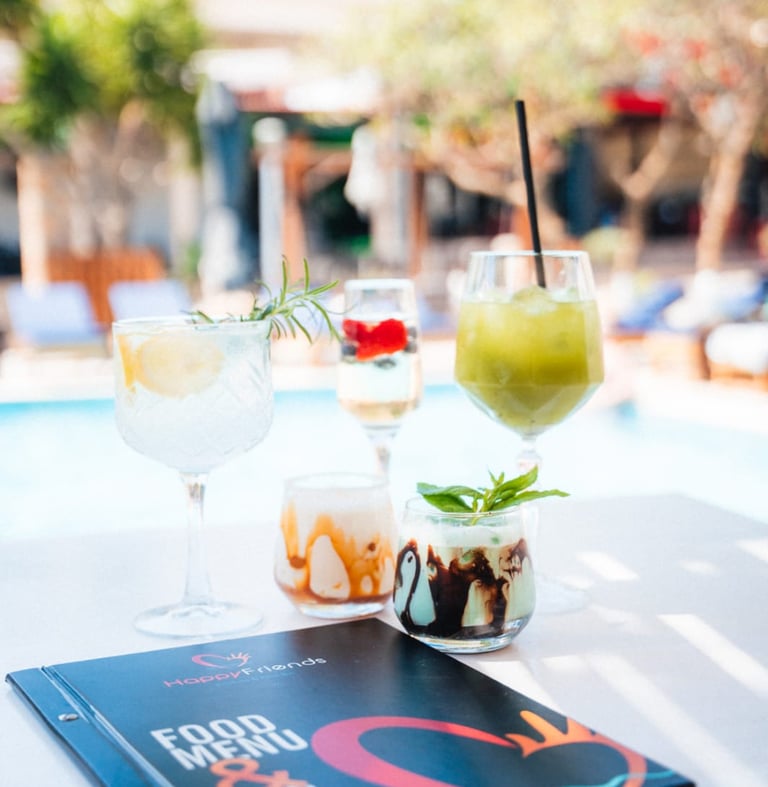 Refreshing summer cocktails and a bar menu on a table by a tropical resort swimming pool.
