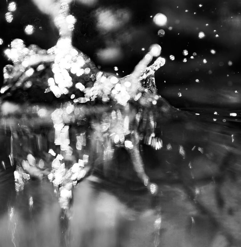 Black and white abstract photography showing a water splash with sparkling droplets and bokeh light.