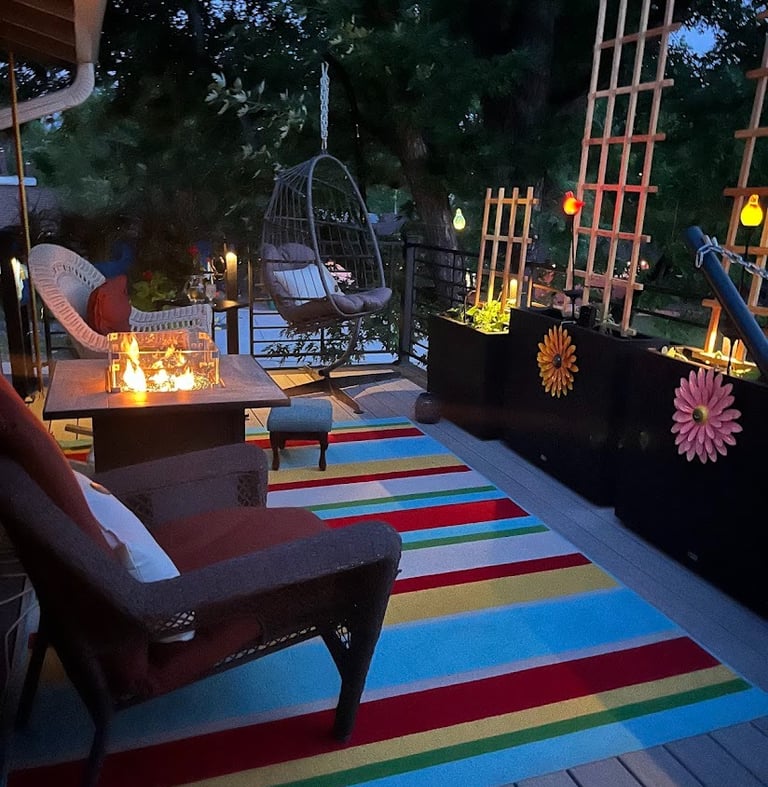 Cozy backyard deck at night featuring a modern gas fire pit table, hanging egg chair, and colorful striped rug.
