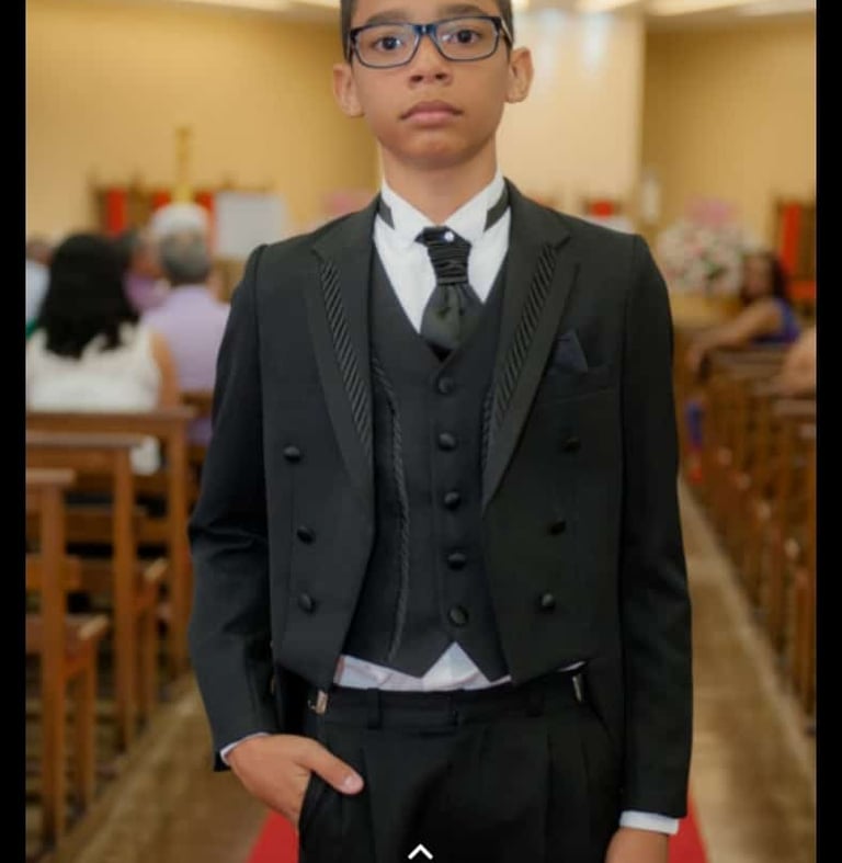 Foto de um garoto vestido com um terninho fino, de otima qualidade.