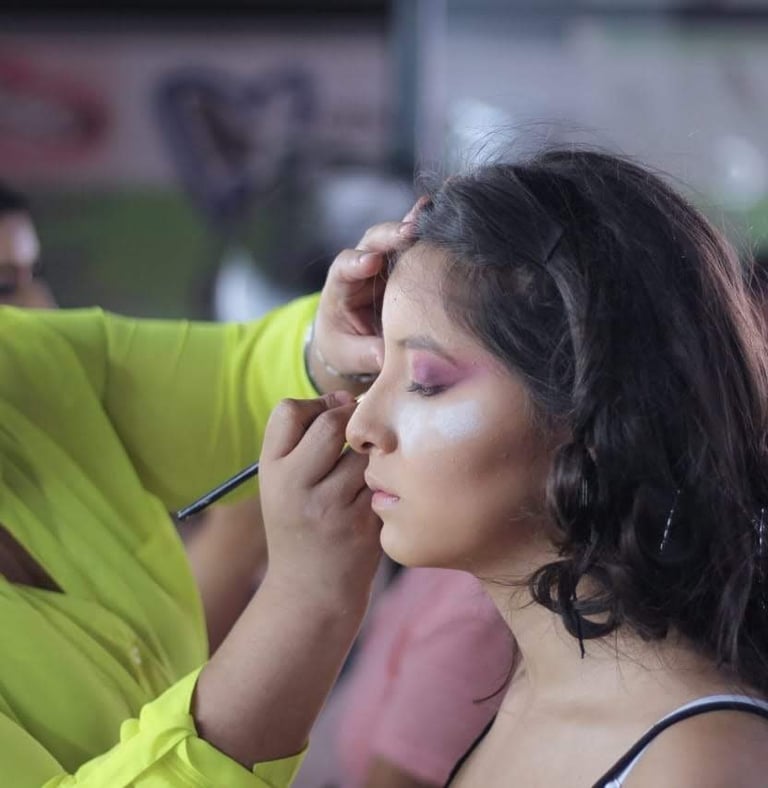 Maquilladora profesional aplica sombra de ojos morada a una mujer joven para un evento especial.