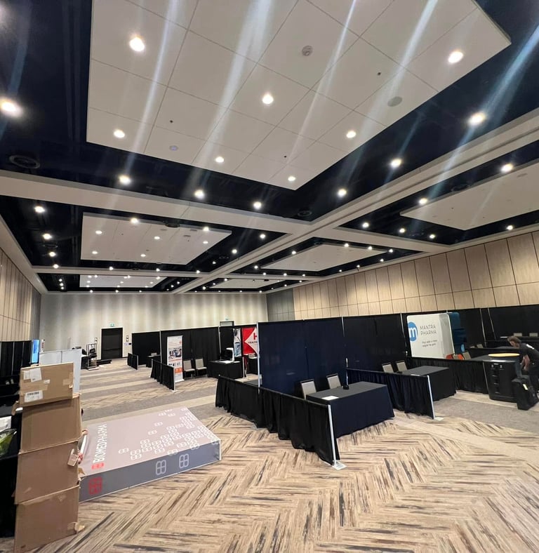 Empty convention hall setup with black drapes, exhibitor booths, and modern ceiling lighting.