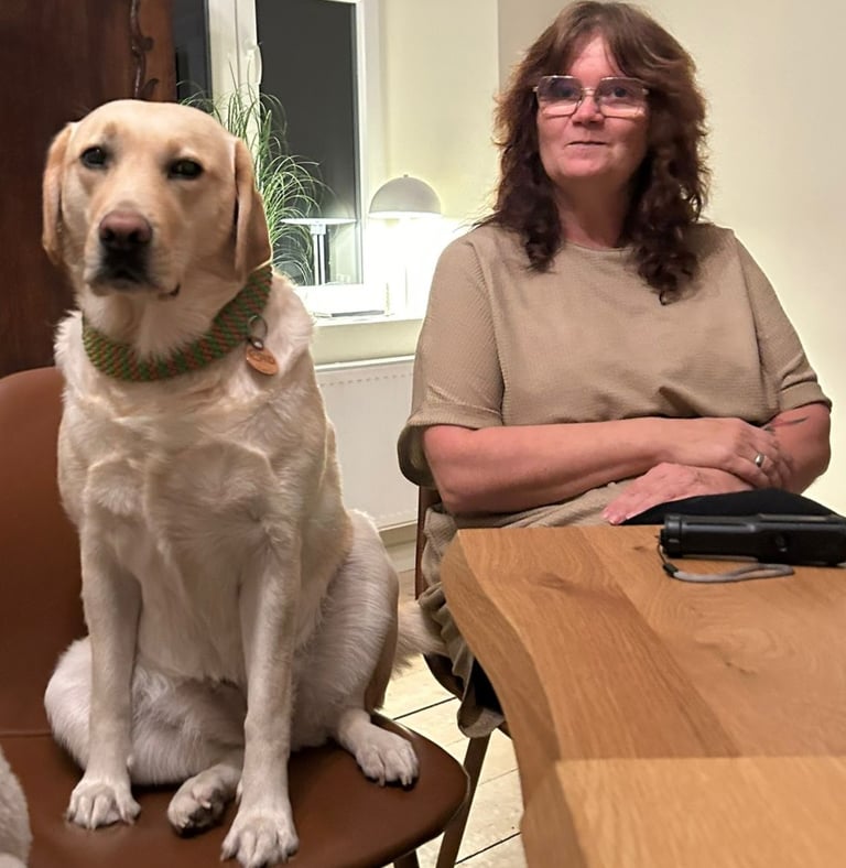 Carmen und ihre Labradorhündin Bonny sitzen an einem Tisch. Auch Bonny sitzt auf einem Stuhl.
