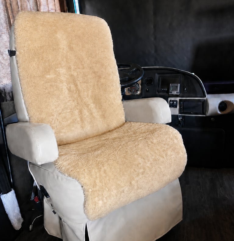 Beige sheepskin seat cover installed on a swivel captain chair inside a luxury RV motorhome cabin.