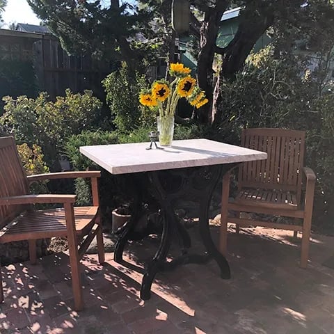 Exterior table with base made from cast iron legs from vintage paper cutter holding a white marble tabletop.