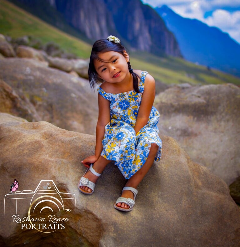 a little girl sitting on a rock in a mountain posing for portrait