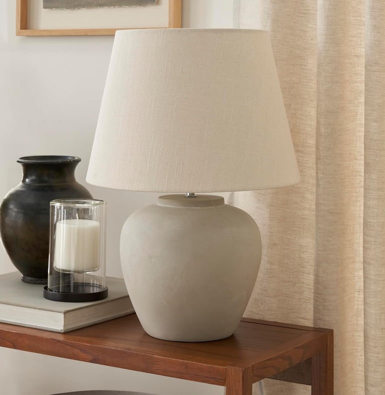 Modern concrete table lamp with a beige linen shade on a wooden side table with decor.