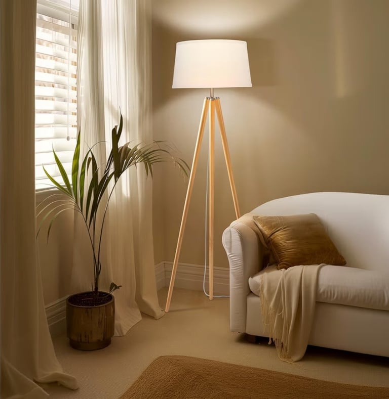 Modern tripod floor lamp with wooden legs and white shade in a cozy living room nook.