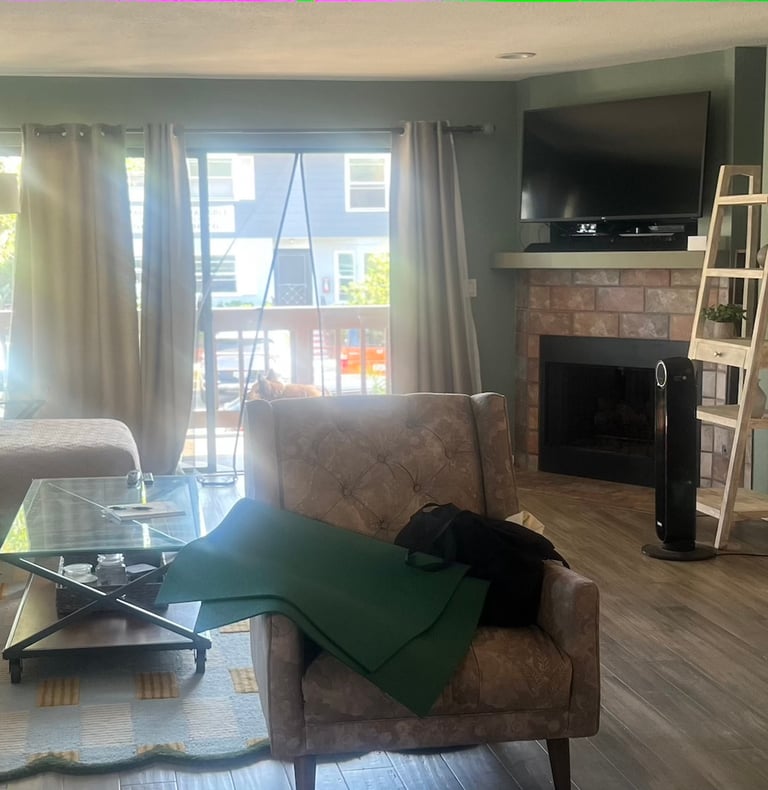 before staging: a clutered room with chair, copy table and sofa. fireplace and wood ladder
