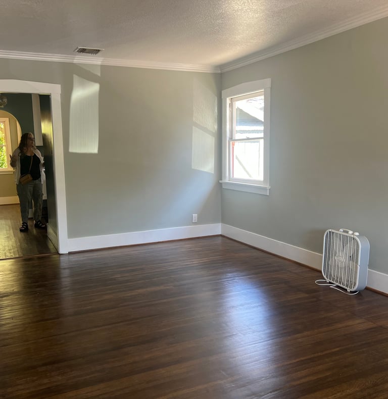 before staging: a person standing in a vacant room with a fan and a fan