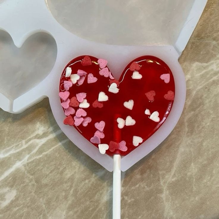Red heart-shaped lollipop with pink and white heart sprinkles in a silicone candy mold.