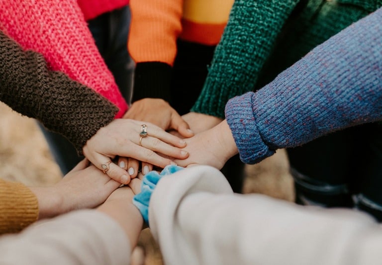 Diverse group of woman in colorful sweaters joining hands in a huddle for community support.