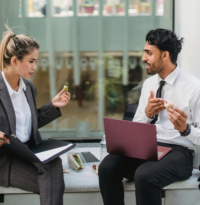 2 people in business meeting while eating sandwich outside with laptop