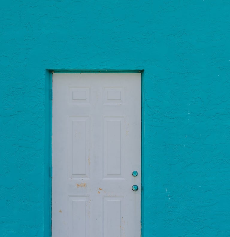 a white rusty door against a teal blue building
