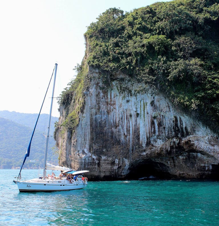 a sailboat in the water near a cliff off the coast of Puerto Vallarta