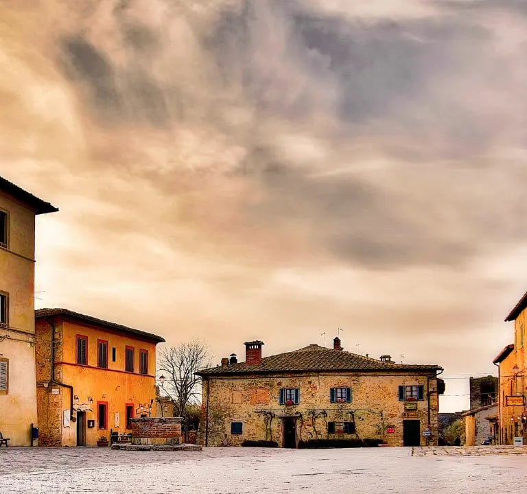 Piazza Roma in Monteriggioni, Tuscany – medieval square with stone buildings and warm sunset sky ins