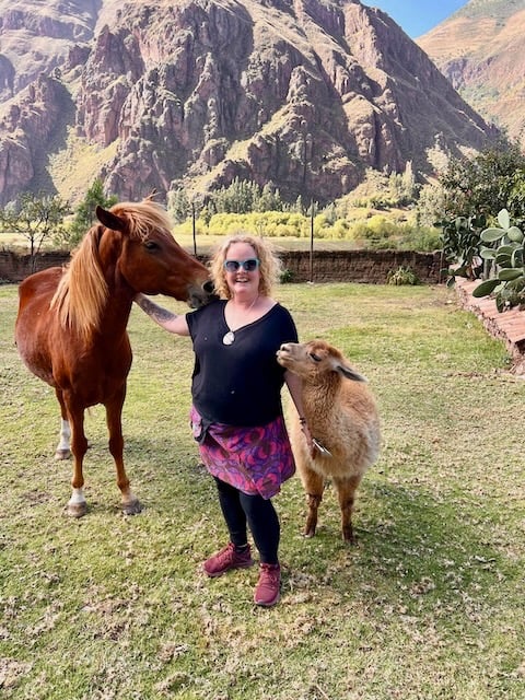 Sunni Dawson smiling with a horse and alpaca in mountains