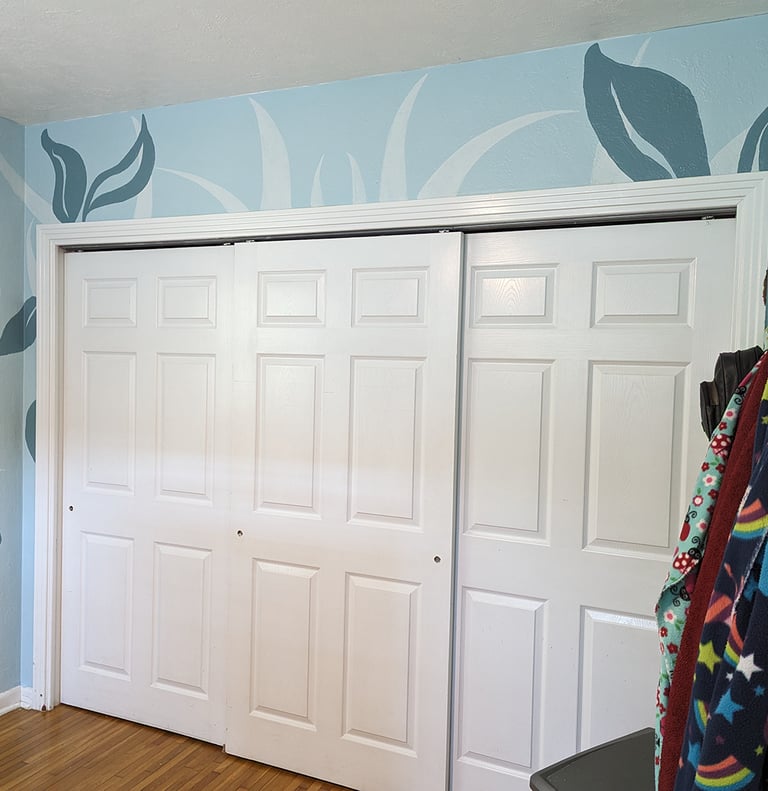 Painting colorful shapes on a wall mural surrounding closet doors.