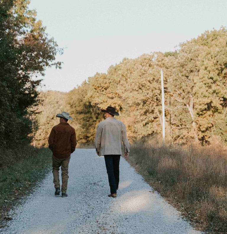 two men in cowboy hats and boots walking away down gravel road