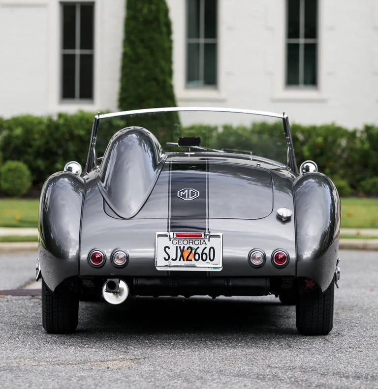 Photograph of a silver and black 1958 MG MGA from the rear in a elegant garden setting