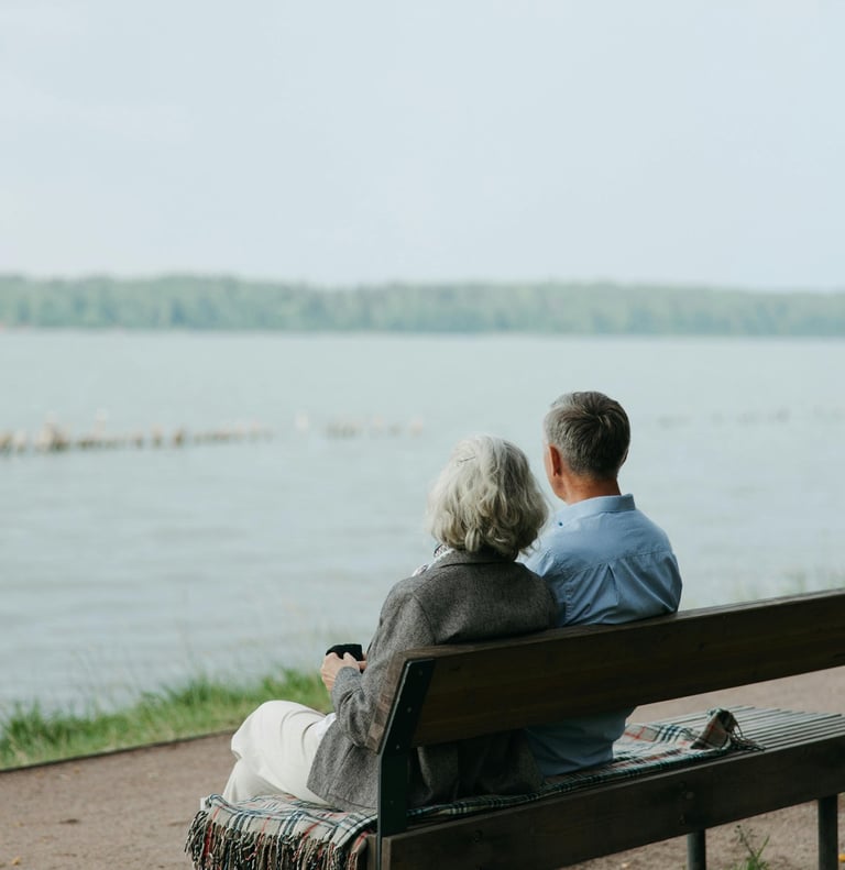 a man and woman sitting on a bench in front of a lake